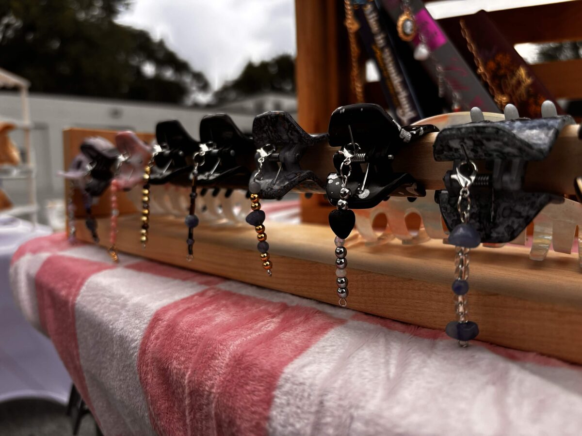A row of marbled claw clips clamped along a wooden rail at a market stall, each hung with a strand of beads.